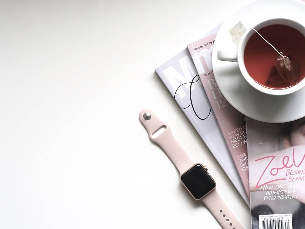 Pink Apple watch sitting next to a few magazines and a cup of tea