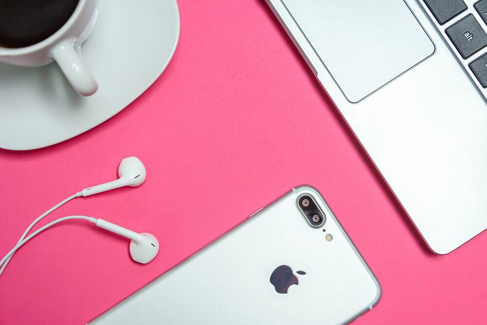 A silver iPhone with earplugs on a shocking pink desk