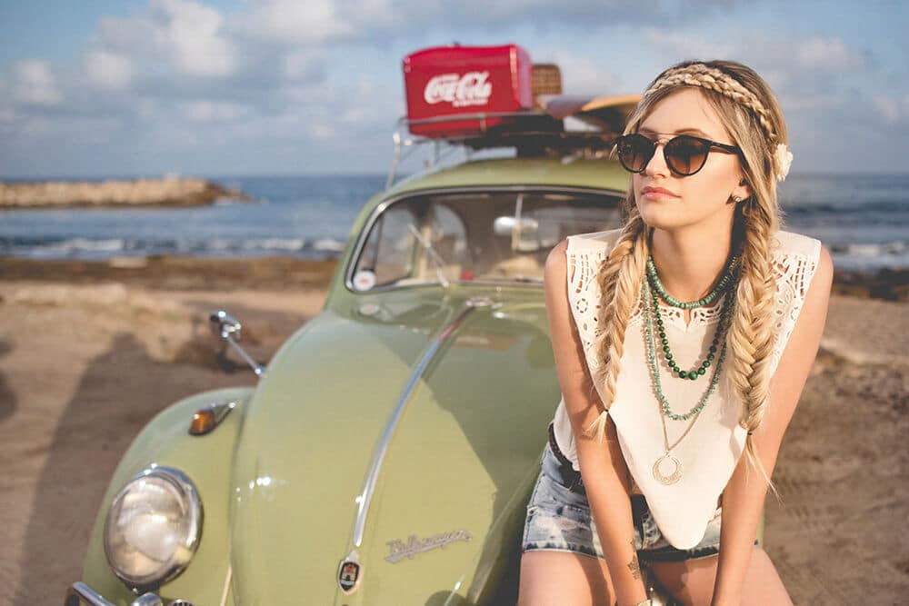 Blonde girl sitting on the hood of a Volkswagen Beetle on a road trip