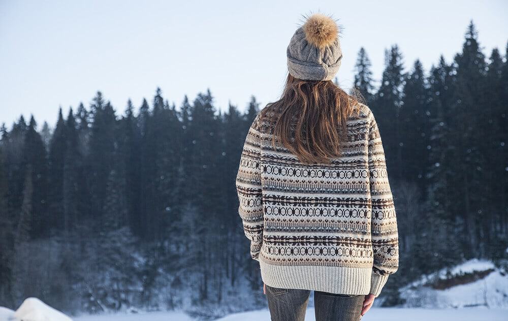 Ragazza con indosso maglione e cappello in lana con ponpon osserva la foresta innevata a Banff