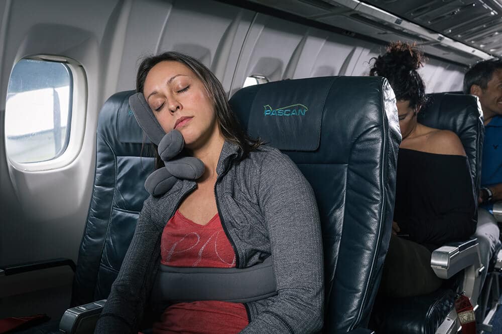 Donna dorme in aereo usando un cuscino da viaggio