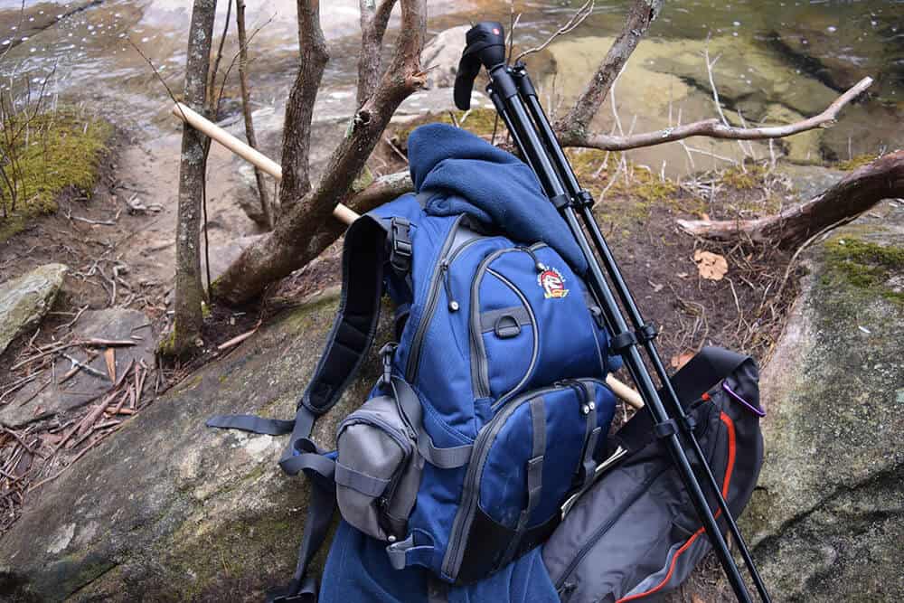 Hiker's backpack and a tripod laying on a rock in the forest