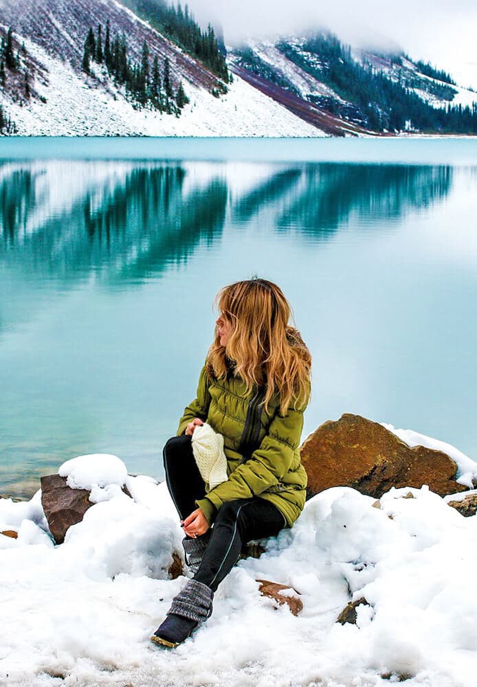 Woman sitting next to a lake in Switzerland in winter wearing thermal clothes