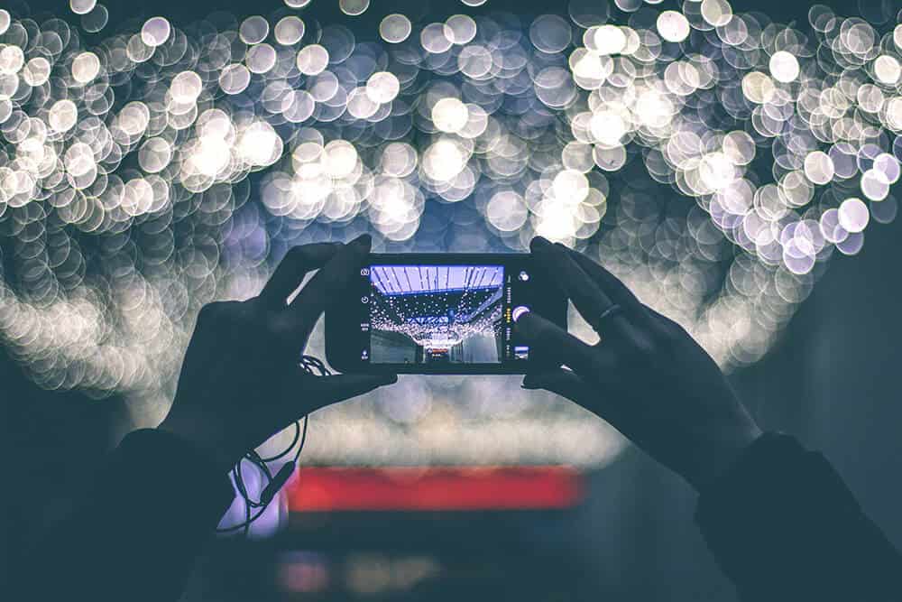 Woman taking a picture of lights at a Christmas market in Europe with her phone