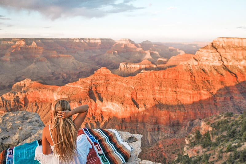 Ragazza seduta su una coperta di Nativi Americani osserva il tramonto al Grand Canyon
