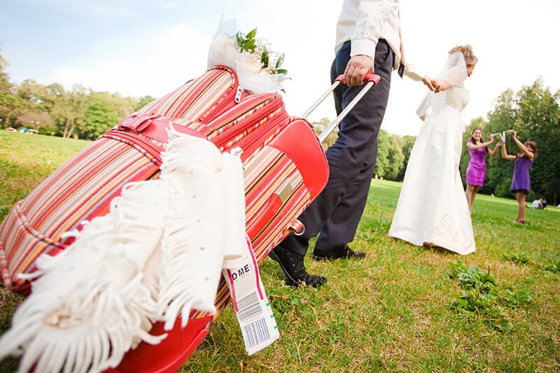 Coppia di sposi trascina una valigia rossa per andare in viaggio di nozze