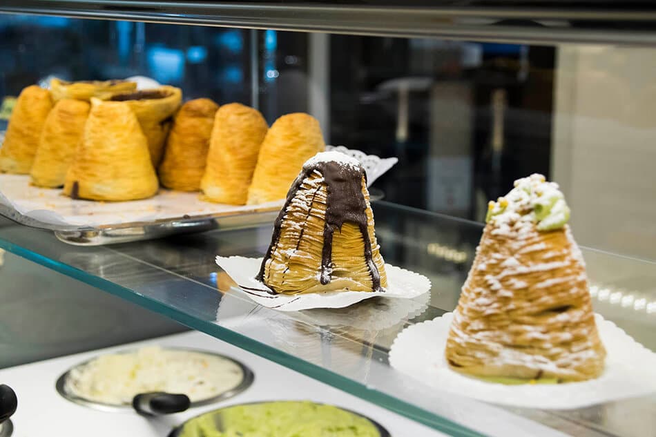 Vetrina di una pasticceria con sfoglia campanella ricoperta da cioccolato fuso e zucchero a velo