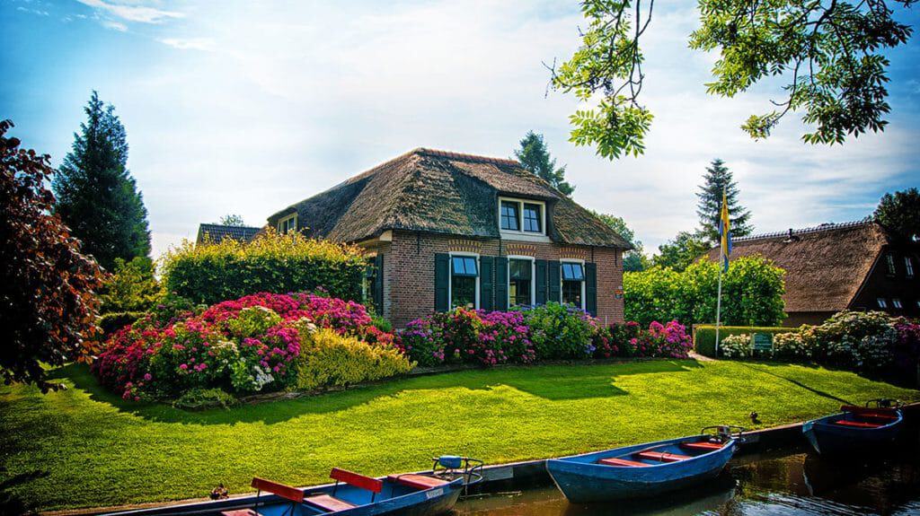 Casa con tetto di paglia a Giethoorn, circondata da cespugli fioriti e barchette