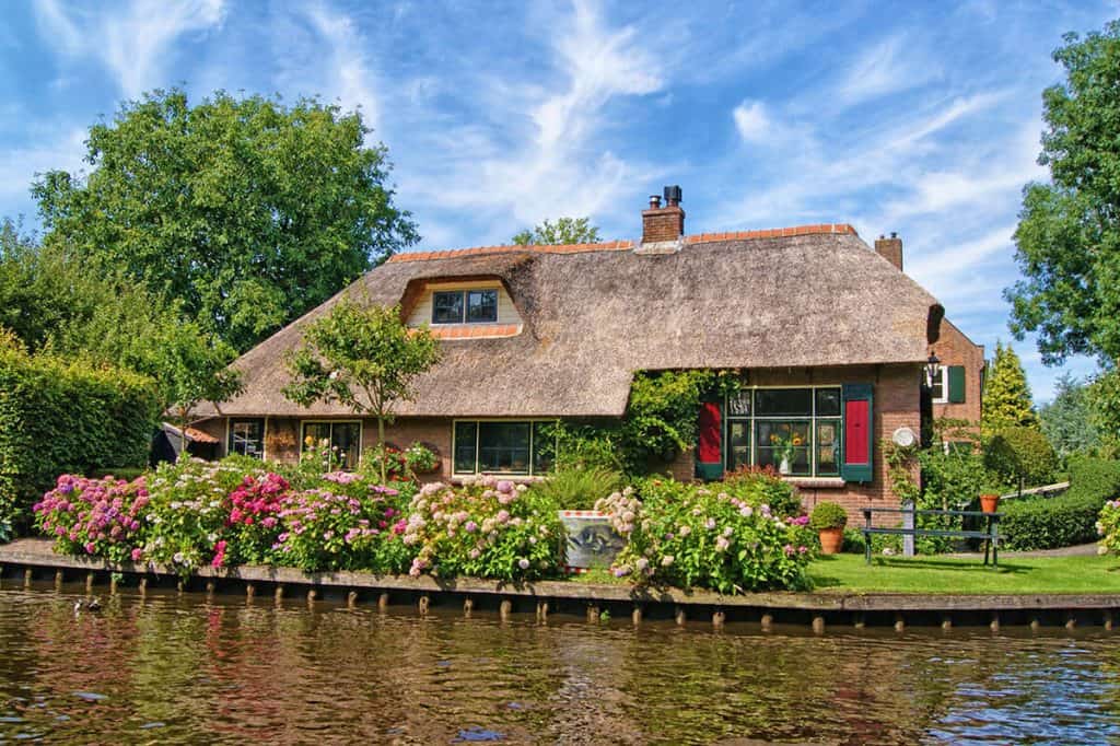Primo piano di una casa tradizionale olandese a Giethoorn circondata da alberi e arbusti in fiore