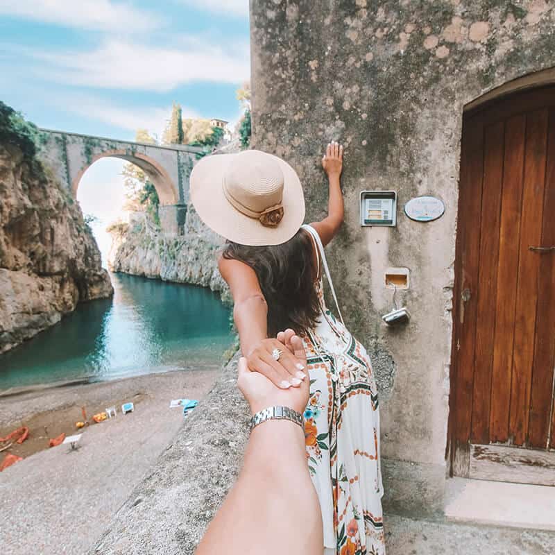 Girl wearing a summer hat looks over to the Furore Bridge on the Amalfi Coast while holding her boyfriend's hand