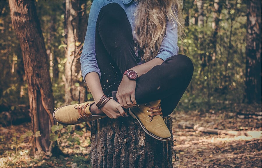 Girl sitting on a log in the forest and showing her Autumn boots
