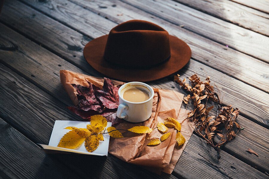 Un cappello, una tazza di caffè e foglie d'autunno su un parquet da esterno