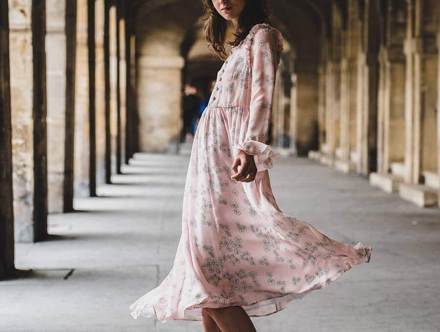 Una donna lascia svolazzare l'abitino rosa romantico che indossa sotto porticati italiani