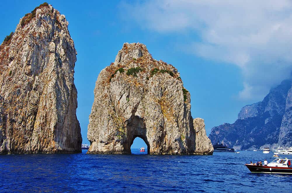 The majestic Faraglioni in Capri, one of the most romantic places in Italy, with boats approaching them