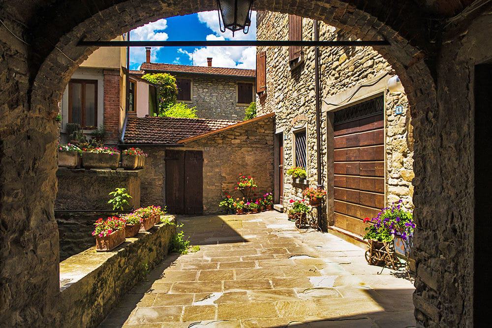 Arco in pietra che si apre su un cortile antico pieno di vasi di fiori