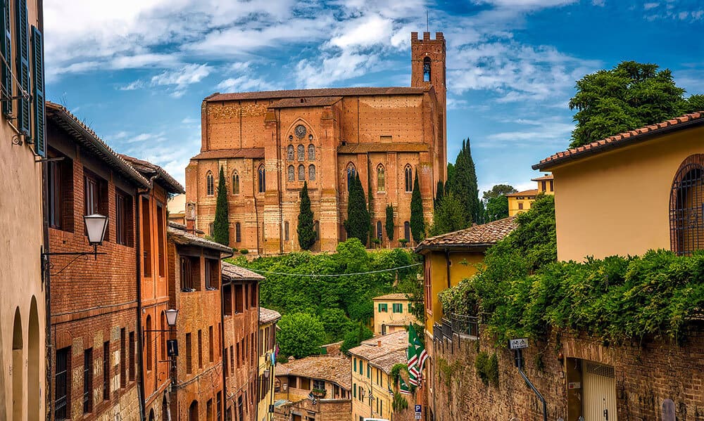 Panoramica di una stradina di Siena con case antiche e una chiesa sullo sfondo