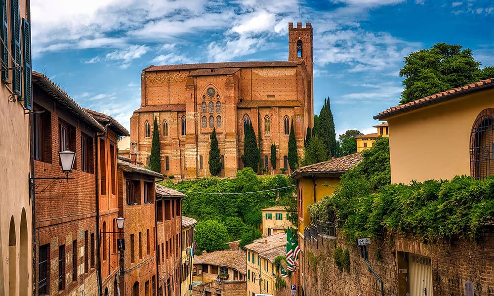 Narrow street in Siena (Italy) lined with brick houses, leading to an ancient church 