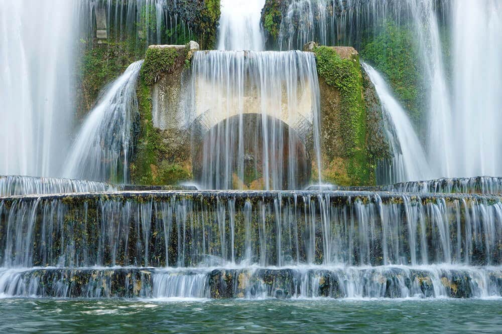 Tall waterfall with a stone arch at Tivoli Gardens in Italy