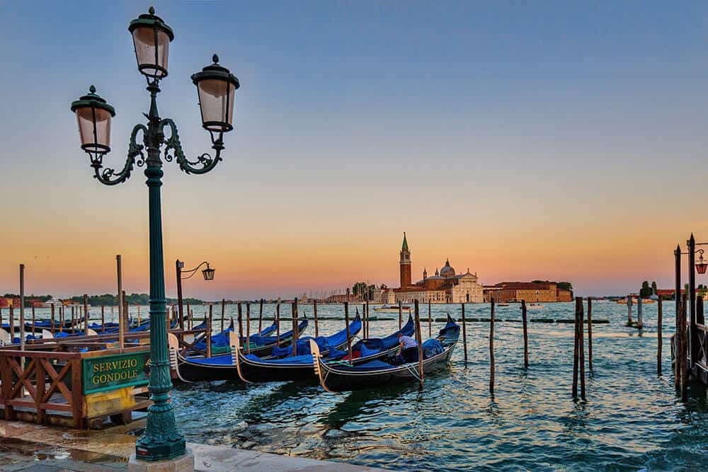 Gondolas in the canal next to a lamplight with a romantic sunset over Venice in the background
