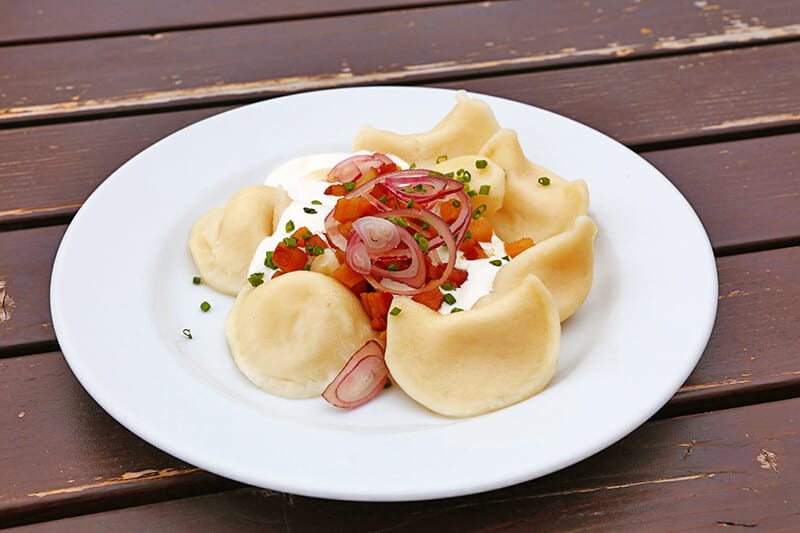 Pierogi polacchi bolliti e serviti con cipolle, pancetta e panna acida