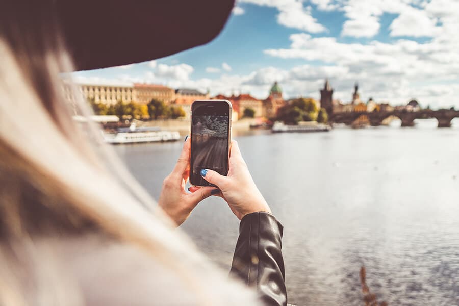 Where to stay in Prague  | Blonde girl taking a picture of the Vlatava river with her iPhone