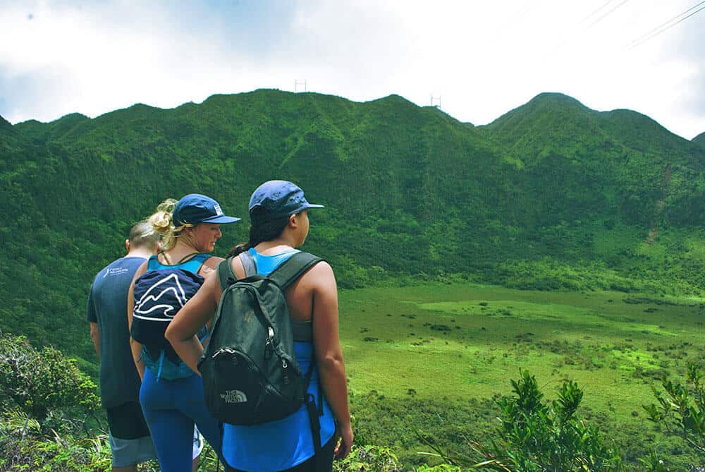 Planning a trip to Hawaii on a budget - Group hiking on Oahu, green mountains in the background