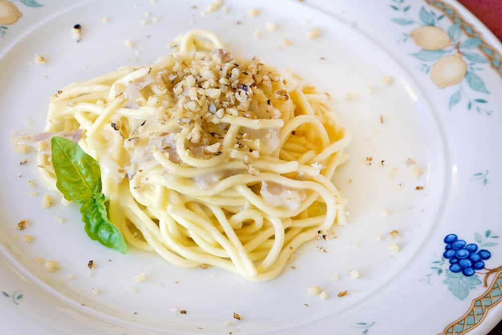 Italian spaghetti cacio e pepe on a plate with chopped walnuts to decorate the dish