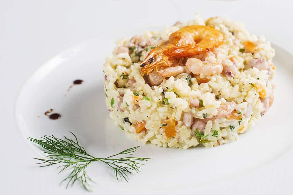 Un piatto di risotto con gamberi, pomodorini gialli e aneto