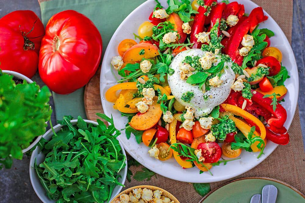 Italian traditional mozzarella di bufala on a plate with bell peppers salad and arugula