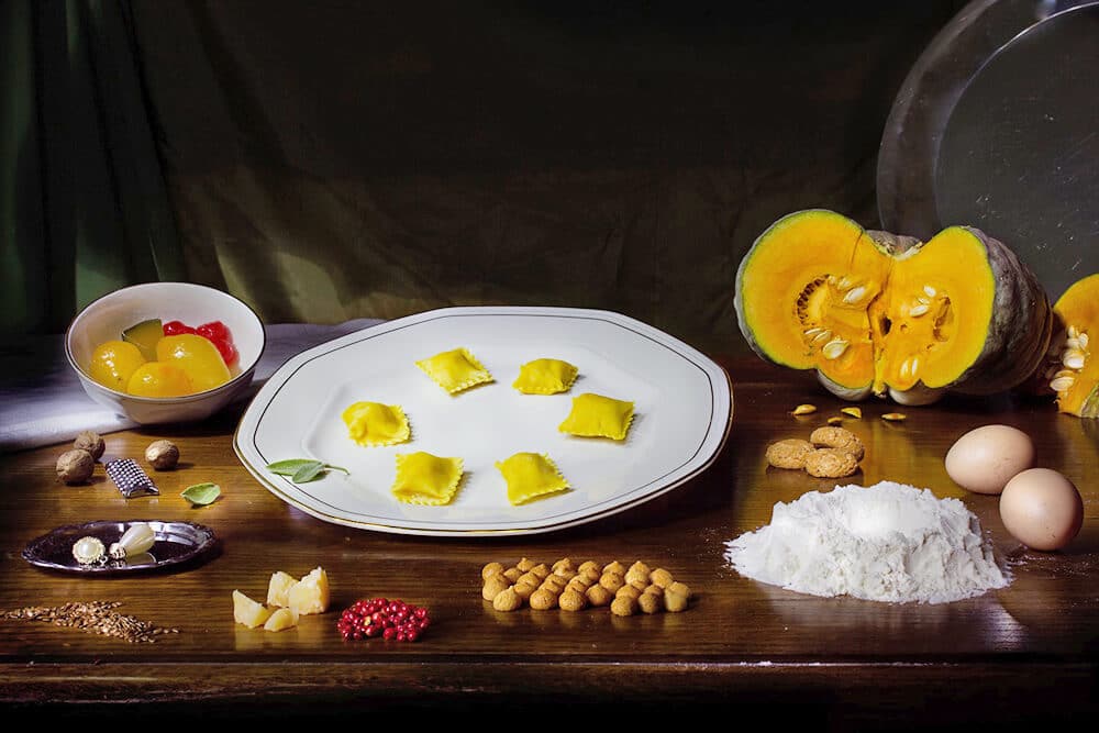 Traditional Italian pumpkin ravioli on a table with pumpkins, nuts and flour