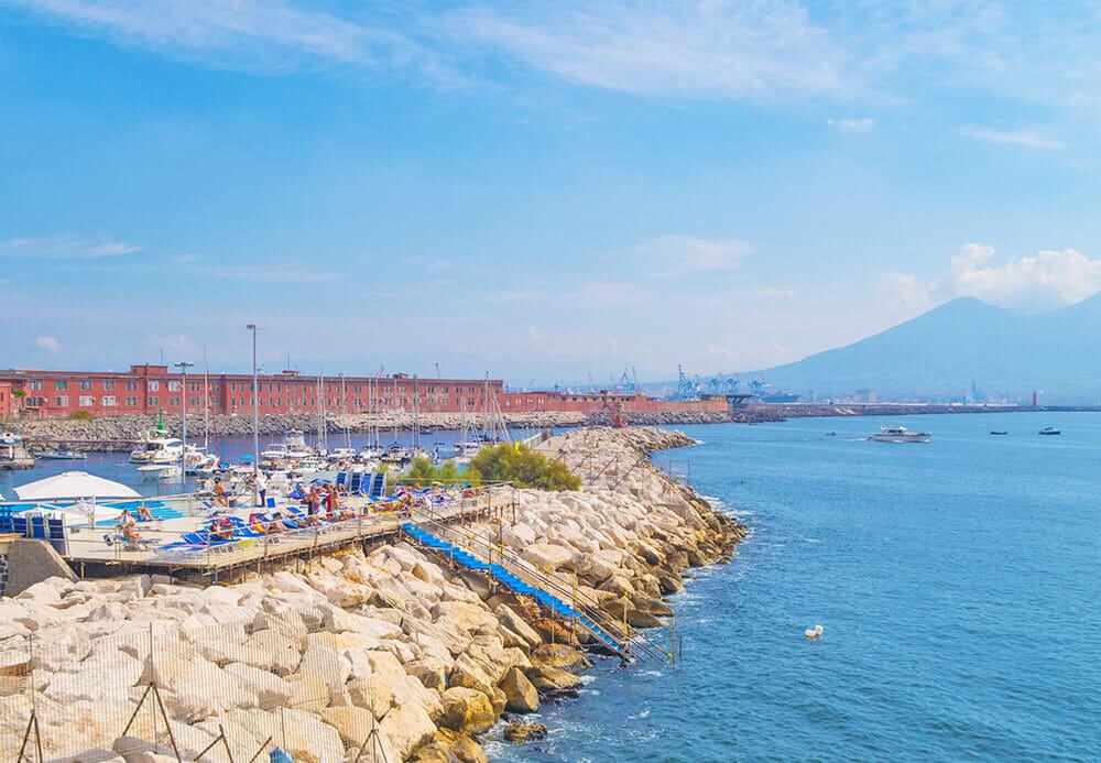 Una giornata di sole a Napoli con tante persone che si abbronzano sugli scogli