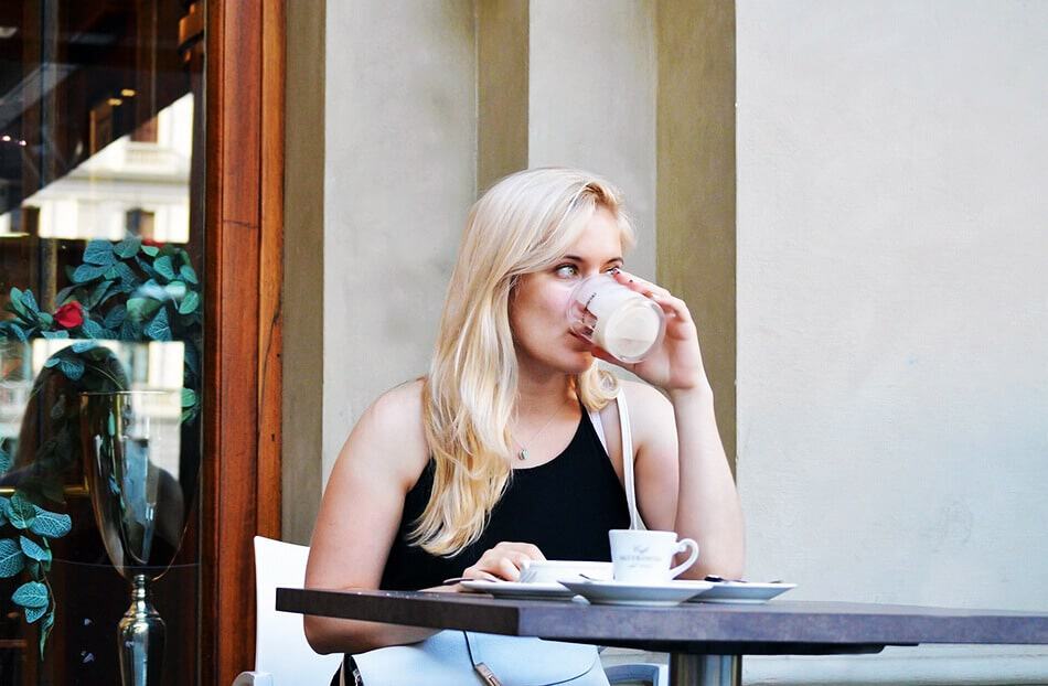 Caffè napoletano - Donna bionda seduta al tavolino di un bar beve un bicchiere di acqua prima di prendere il caffè