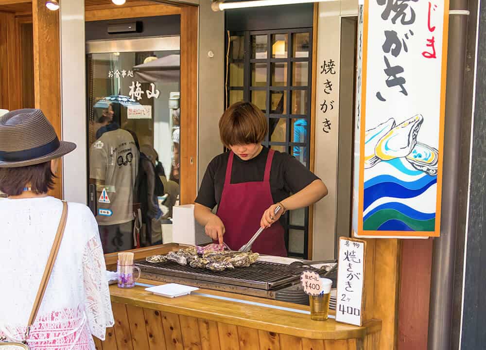 Things to do in Miyajima | Vendor grilling and opening an oyster at Omotesando street in Miyajima