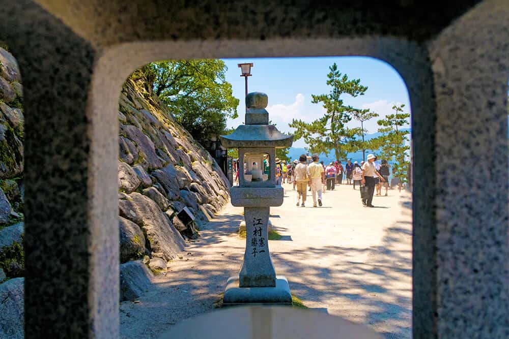  Viaggio in Giappone | Strada costiera pedonale a Miyajima vista attraverso una lanterna in pietra