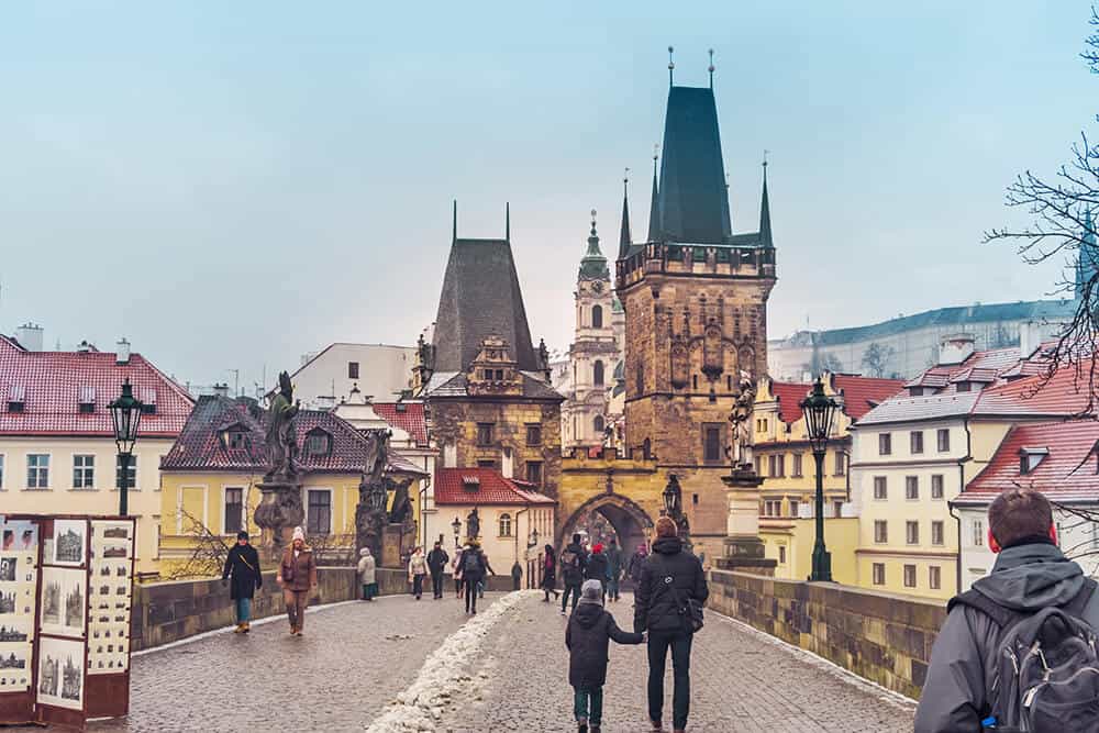 People crossing Charles Bridge in Prague with snow on the street