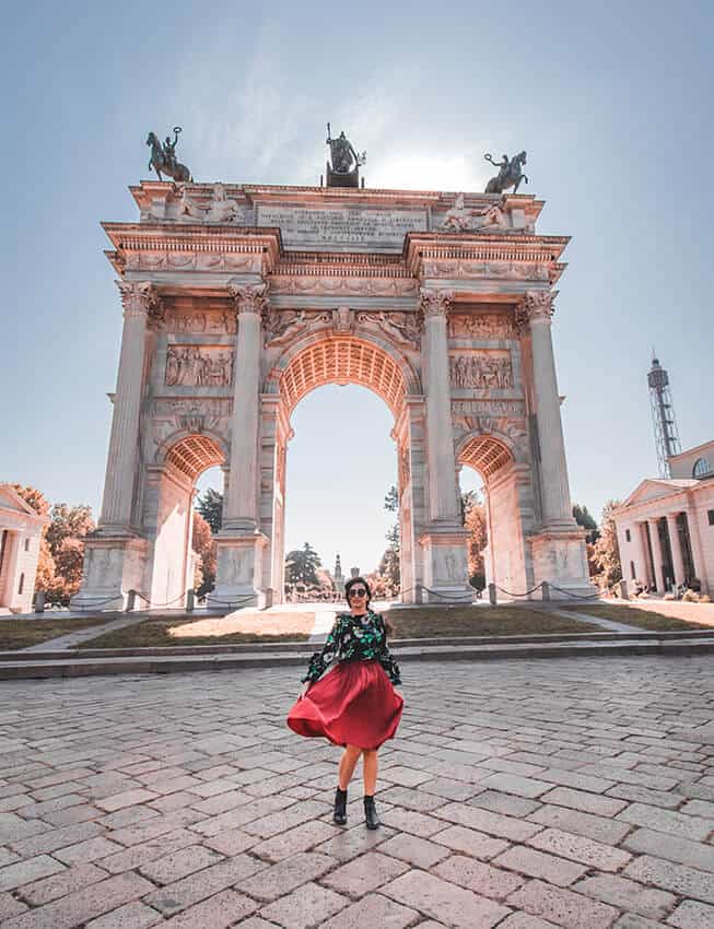 Girl wearing a red skirt twirls in front of a marble arch in Milan (Italy)