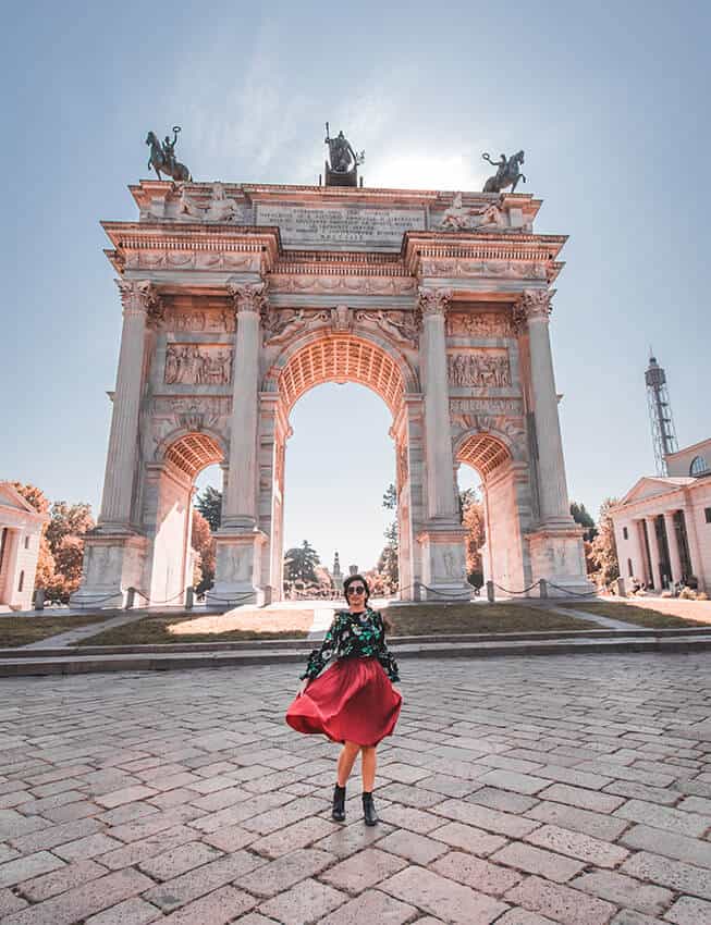 Girl wearing a red skirt twirls in front of a marble arch in Milan (Italy)