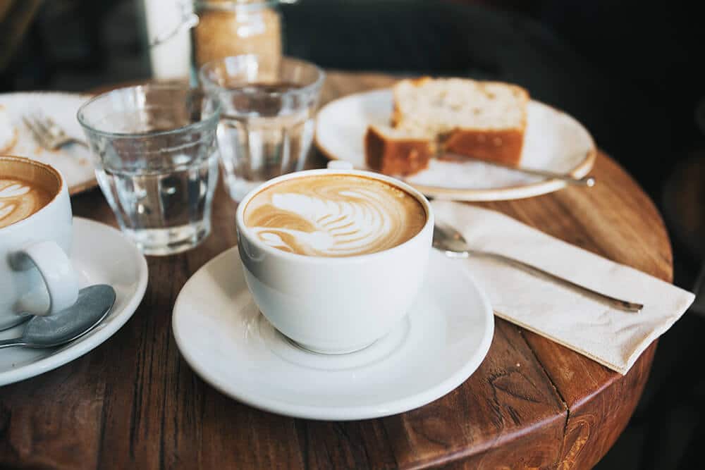 Un cappuccino con schiuma e due bicchieri d'acqua serviti al tavolino di un bar