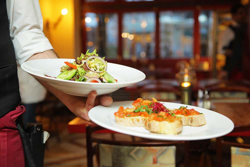 A waiter serving Italian bruschetta and a salad in Naples (Italy)