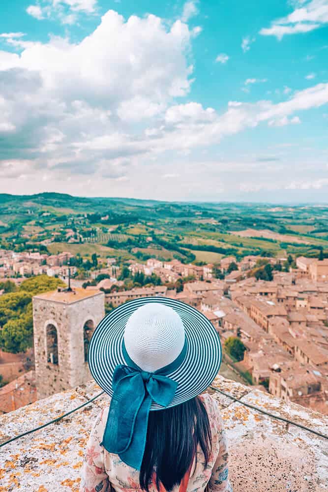 Ragazza con cappello osserva una città in Toscana dall'alto