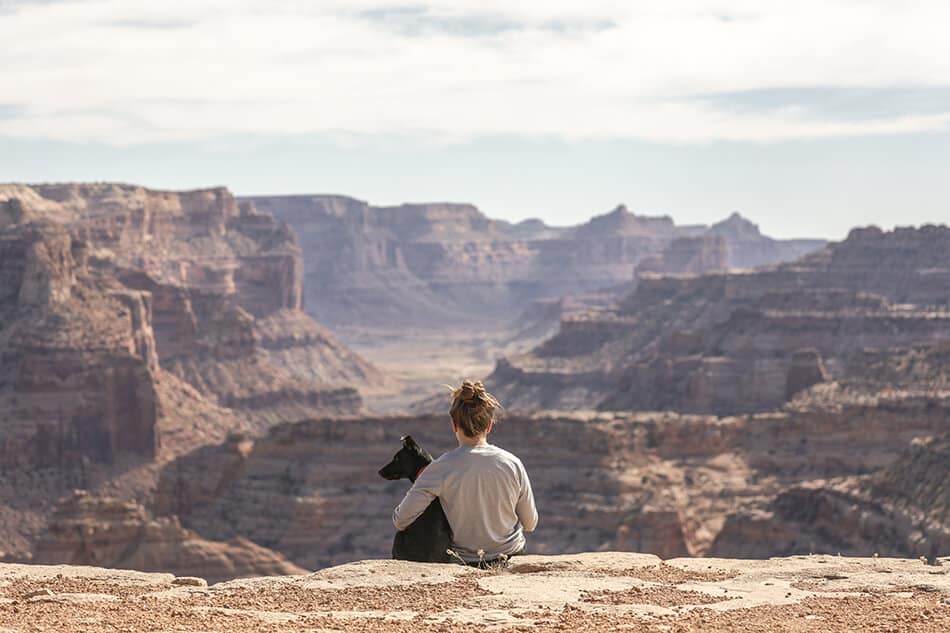 Ragazza abbraccia il suo cane seduta su una roccia durante una escursione al Grand Canyon