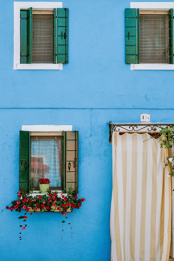 Puikus mėlynas namas su žaliais langais ir raudonomis gėlėmis Burano mieste, netoli Venecijos (Italija)