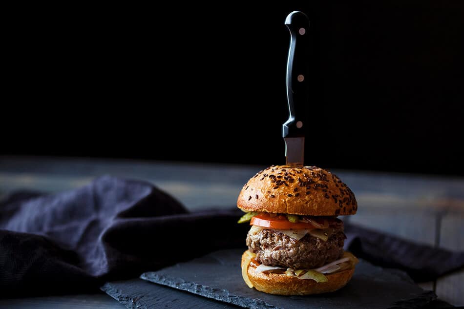 A delicious Angus burger on a black table stabbed with a knife 