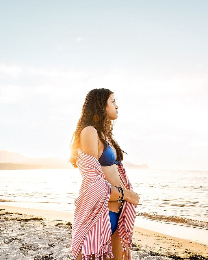 Ragazza con indosso un bikini blu e un pareo a strisce osserva il tramonto su una spiaggia della Costiera Amalfitana