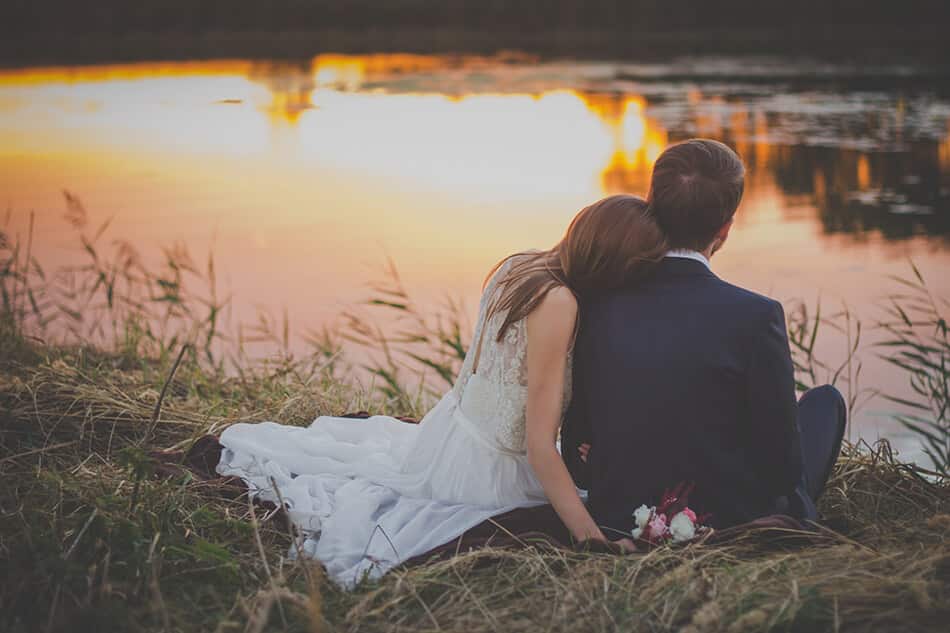 Coppia di sposi seduti sulle rive del fiume al tramonto