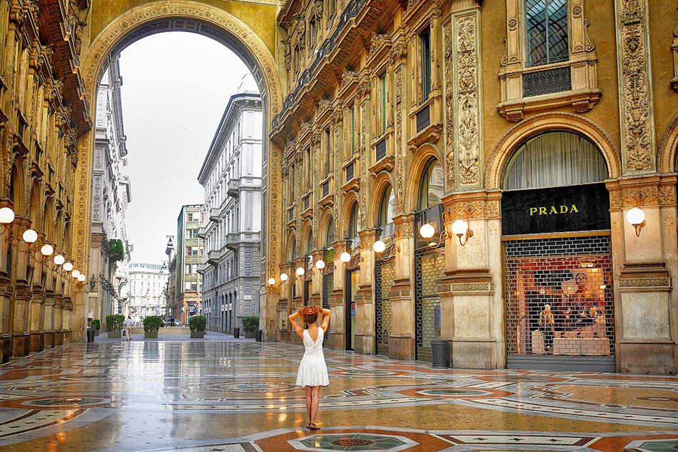 Idea su cosa mettere in valigia: una ragazza indossa un abitino bianco davanti a un negozio di Prada a Milano