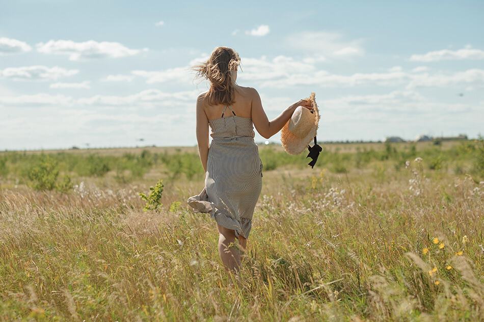 Woman walking with a dress and a floppy hat in the Tuscany countryside in summer