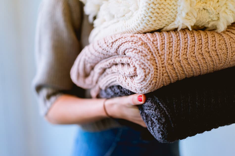 Ragazza porta tre maglioni in lana scozzese piegati