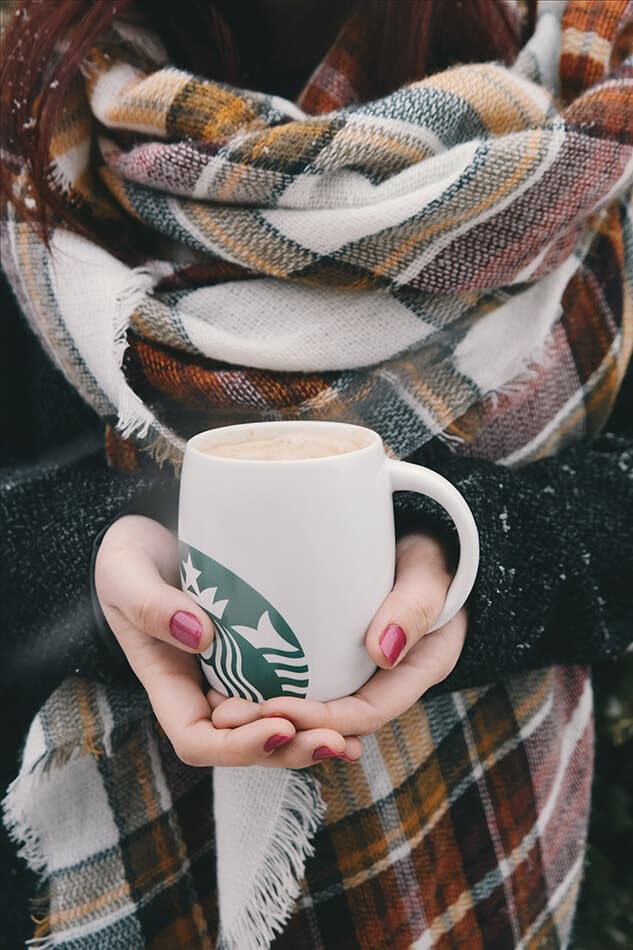 Woman holding a Starbucks mug with a tartan scarf around her neck