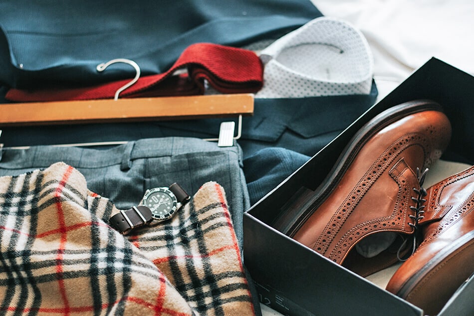 A tweed scarf, leather shoes and men's clothing on a bed